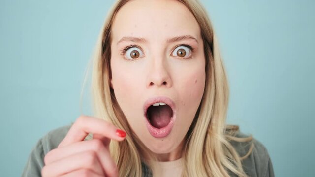 A shocked woman is looking to the camera standing isolated over a blue background in the studio