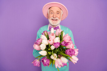 Portrait of satisfied aged person hands hold flowers beaming smile look camera isolated on purple color background