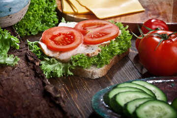 Fototapeta na wymiar turkey meat sandwich with tomatoes, cheese, green salad and cucumbers on dark wooden table background