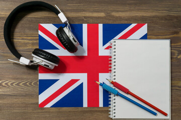 Headphones, a spiral notebook and two black-graphite pencils are lying on the flag of Great...