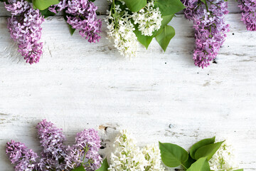 Beautiful lilac on a light wooden background. Purple and white flowers are arranged around the perimeter of the frame. Place for inscription, soft focus