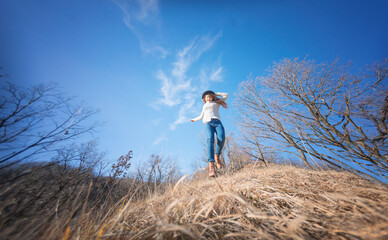 Naklejka na ściany i meble Young happy cheerful woman in hat jumping on blue sky background in spring forest