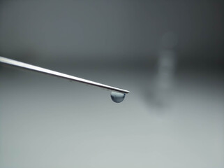 Syringe needle with a drop at the end close-up on a light background