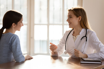 Friendly young female therapist in white uniform talking to smiling patient at health examination...