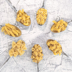 Various pasta on spoons on a white stone background. different sort pasta on spoons laid out in a circle.