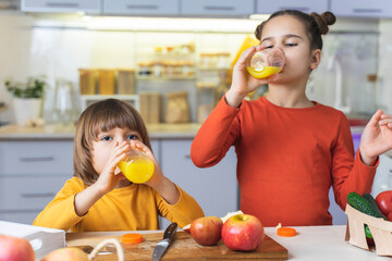Children drink fresh organic orange juice from a bottle at home. Kids holds a bottle of juices and eating apple. Concept of healthy and delicious food for the family. Healthy living © Alex Desanshe