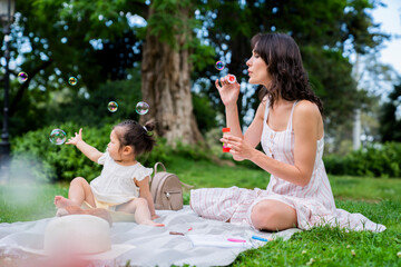 Obraz premium Mother and daughter having fun with soap bubbles outdoors