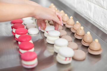 Close up cropped image of female hands, connecting the two halves shells of macarons, decorated with jam and ganache
