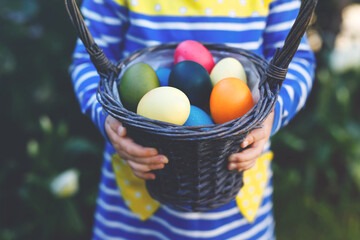 Close-up of of hands of toddler holding basket with colored eggs. Child having fun with traditional...