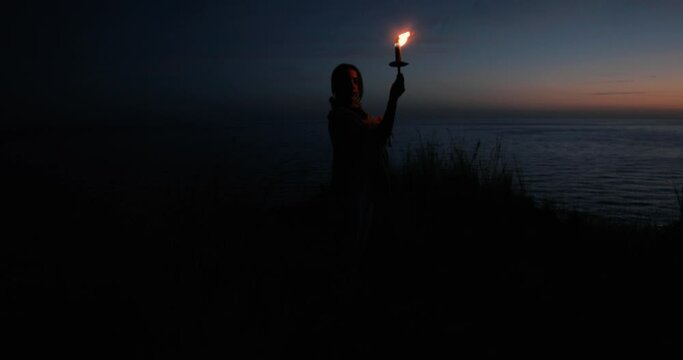 Ragazza con fiaccola di fuoco cammina di notte vicino all'oceano prima del tramonto