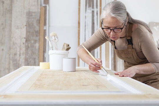 Wood Crafts, Woman Artisan Carpenter Painting With Brush And Paint Jar White The Door In Workshop, Wearing Overall And Eyeglasses, Interior Designer, Restoration, Diy And Handmade Works Concept