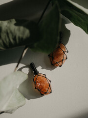 Pendants made of natural sun stone lie on a white background next to eucalyptus leaves