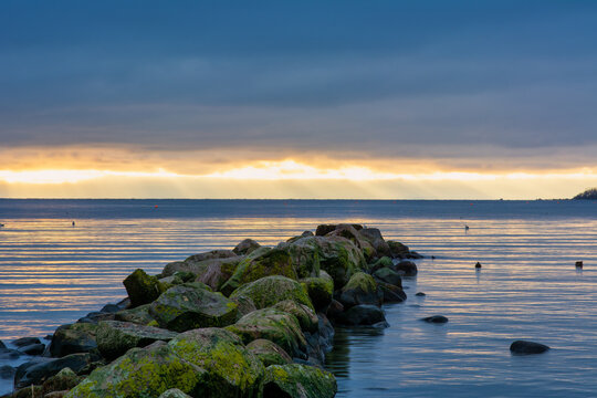 A beautiful sunset over the green boulders on a wave breaker. Photo from Hallevik, Blekinge county, Sweden