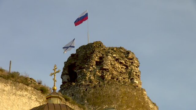 Crimea, Sevastopol. Destroyed tower of the Kalamita fortress in Inkerman. Tower with Russian and Andrew flags. In foreground is tdome withgolden orthodox cross of active monastery. 