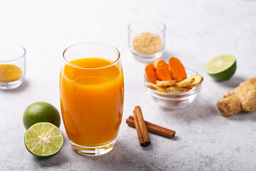 Healthy drink from turmeric and ginger roots and lime in a glass on white concrete background.