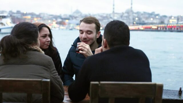 Turkish people in Istanbul drinking cay, traditional tea in Turkey - Group of friends sitting by the river in Istanbul and enjoying time together in the evening - Friendship and lifestyle concepts