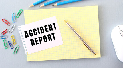 ACCIDENT REPORT is written on a piece of paper that lies on a notebook next to office supplies.