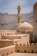 Minaret, dome and walls of medievel arabian fort of Nizwa, Oman. Hot day in arabian desert city.