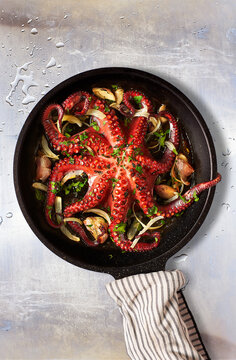 Octopus Lagareiro style dressed with onion and garlics cloves on an aged metallic table. Portuguese cuisine.