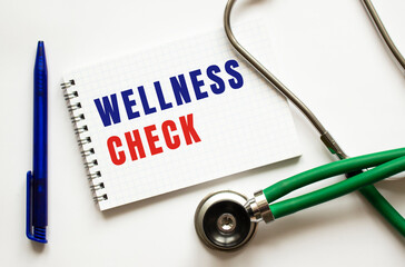 WELLNESS CHECK is written in a notebook on a white table next to pen and a stethoscope.