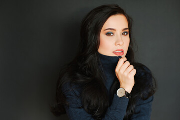 Fashion portrait of pretty young woman wearing turtle neck pullover and watch, posing on dark background