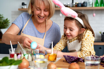 Happy grandma with granddaughter coloring Easter eggs