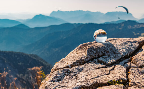 Beautiful alpine summer view with details of a rock with a crystal ball lying on it and a paraglider in the background at the famous Hochfelln summit, Bergen, Bavaria, Germany
