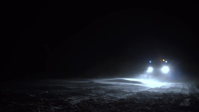 A snowplow clears the Road during a blizzard at night. Winter maintenance and road safety. A strong wind is blowing.