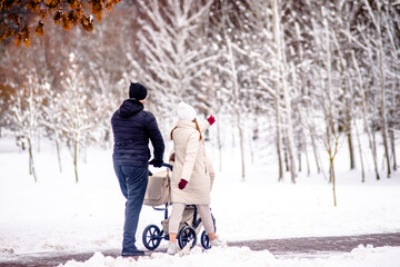 Fototapeta na wymiar A married couple rolls a child in a wheelchair in the winter Park 