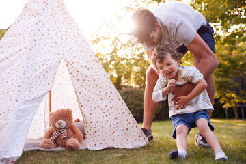 Father And Son Having Fun With Tent Or Tepee Pitched In Garden
