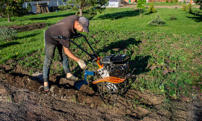 Male in the spring plows the earth in working clothes with a motoblock