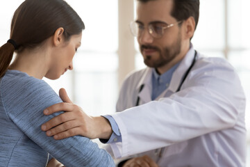 Focus on male doctor's hand lying on frustrated female patient shoulder. Kind young general practitioner comforting confused stressed woman, giving psychological help telling bad news at meeting.