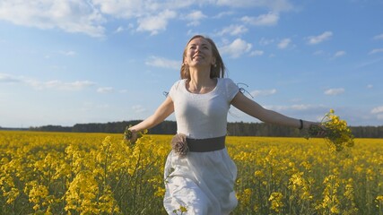 Fototapeta premium A girl in a white dress runs among a rapeseed field.