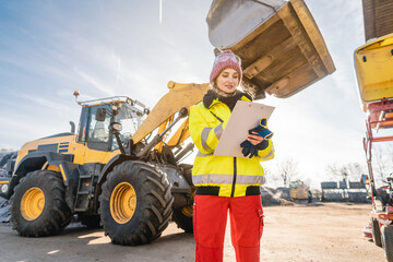 Woman with clipboard in front of construction machinery