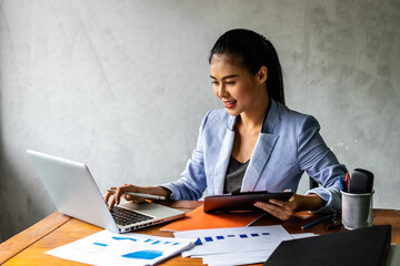 A long-haired Asian business woman is sitting at a desk with a notebook in front of her and looking at documents on the desk