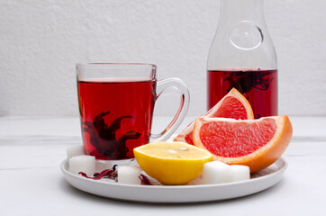 Closeup of glass cup and bottle full of red herbal tea and juicy lemon, grapeftuit, sugar.Fresh tasty herbal tea