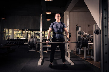 male athlete is holding a barbell in a fitness center, doing his daily workout