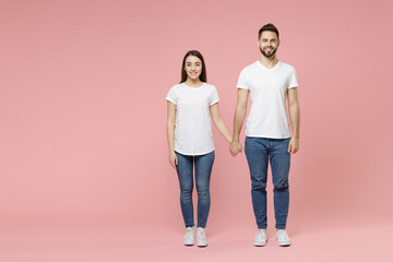 Full body length young cheerful couple two friends bearded man brunette woman in white basic blank print design t-shirts jeans standing posing isolated on pastel pink color background studio portrait.