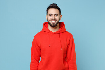 Young caucasian smiling happy cheerful bearded attractive handsome student man 20s wearing casual red orange hoodie looking camera isolated on blue background studio portrait People lifestyle concept. - obrazy, fototapety, plakaty