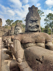 Fototapeta na wymiar Stone sculptures on the bridge in Angkor. Unesco World Heritage Site. Siem Reap Province. Ancient ruins and trees. Cambodia. South-East Asia
