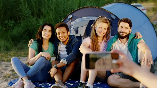 Pictures time at the picnic friend take some photos of a multiethnic group of friends while they sitting down beside of the tent and smiling large. 4k