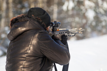 a man of European appearance in the winter forest shoots from a sports crossbow