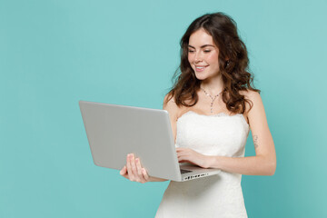 Smiling charming bride young woman 20s in beautiful white wedding dress working on laptop pc...