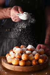 Man sprinkles powdered sugar onBaked castagnole. Street food, round biscuits with sugar for the carnival of Venice. Traditional sweet pastries during the carnival period in italy. Copy space. 