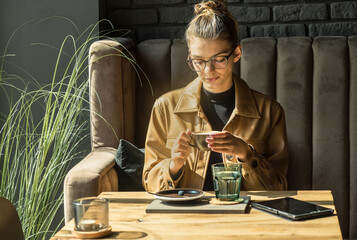Young woman drinking coffee cup and sitting in cafe. Girl in glasses pauses after work.
