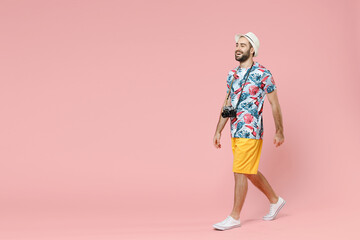 Full length side view cheerful young traveler tourist man in summer clothes hat walking going isolated on pink background studio portrait. Passenger traveling on weekends. Air flight journey concept.