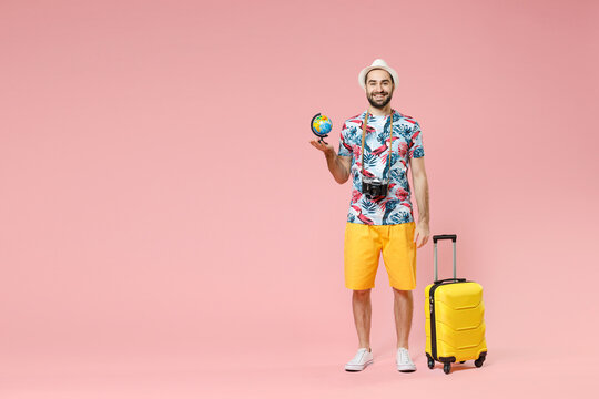 Full length of smiling young traveler tourist man in summer clothes hat hold Earth world globe isolated on pink background studio portrait. Passenger traveling on weekends. Air flight journey concept.