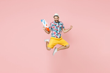 Full length of happy traveler tourist man in summer clothes hat jumping hold toy water gun doing winner gesture isolated on pink background. Passenger traveling on weekend. Air flight journey concept.