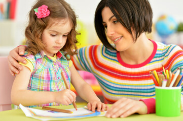 little cute girl with mother drawing at the table at home