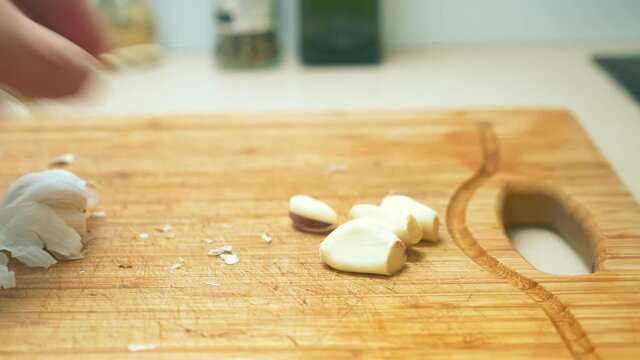 close-up of male hands chopping garlic on a wooden cutting board.